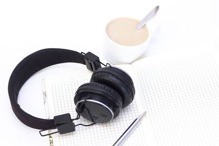 black headphones with a cup of coffee on a white background. notebook with pen on the table