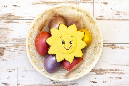 Easter holiday. Colored eggs in a basket. Easter gingerbread cookies sun. on a light wooden...