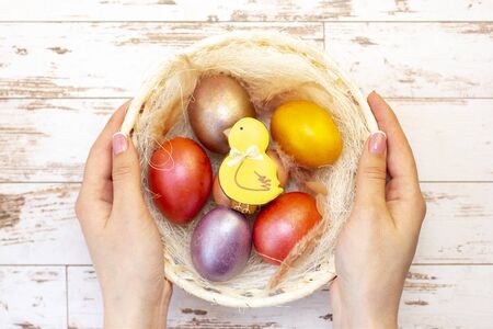 Easter holiday. Colored eggs in a basket. Easter gingerbread chicken in the basket, which is in the hands. on a light wooden background. の写真素材
