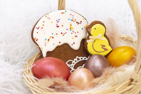 Easter holiday. Colored eggs in a basket. Easter gingerbread chicken and Easter cake. on a light background. の写真素材