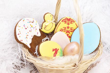 Easter. Colored eggs in a basket. Easter gingerbread egg, Easter cake in a basket. on a light wooden background.の写真素材