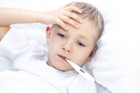 boy lies in bed with a thermometer in his mouth. healthcare concept and sick child, coronavirus, high feverの写真素材