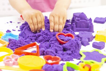 Childrens hands plays kinetic sand in quarantine. purple sand on a white table.の写真素材