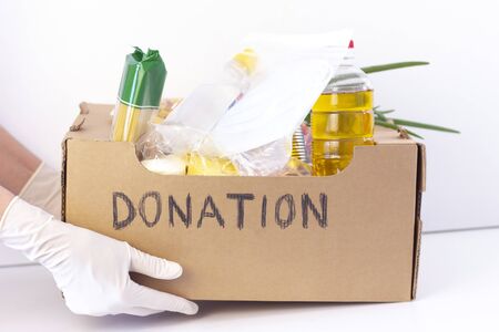 donation box. in hands in rubber gloves is a cardboard box with the inscription donation with food and protective masks and a disinfectant on a white background.の写真素材