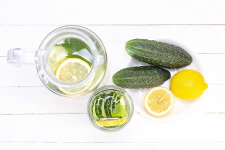 Health care, fitness, healthy eating concept. Fresh cool lemon cucumber drink with water, cocktail, detox drink, lemonade in a glass jug and a glass. cucumbers and lemon on a plateの写真素材