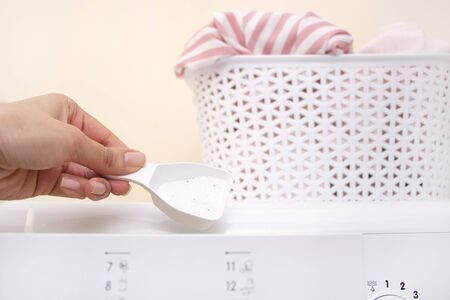 mans hand pours laundry detergent into the compartment of a washing machine. A white basket with dirty laundry. concept of washing clothes and home cleaning.の写真素材