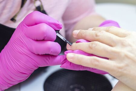 shellac. master in pink gloves puts nail polish on a girl.の写真素材