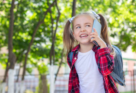 happy schoolgirl with a backpack talking on the phone on the street. in a white T-shirt and a plaid shirtの写真素材