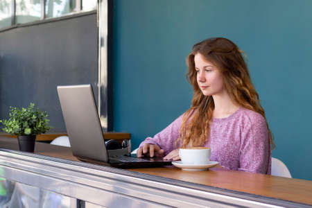 girl works for a laptop. remote work, online. girl in a cafe with a cup of coffee