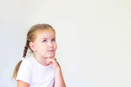 child girl thinks. girl in a white t-shirt holds a finger to her cheekの写真素材