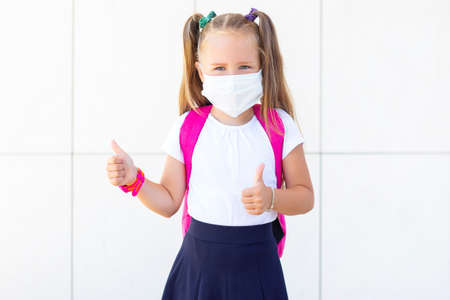 schoolgirl stands with a backpack in a protective medical mask. shows likes
