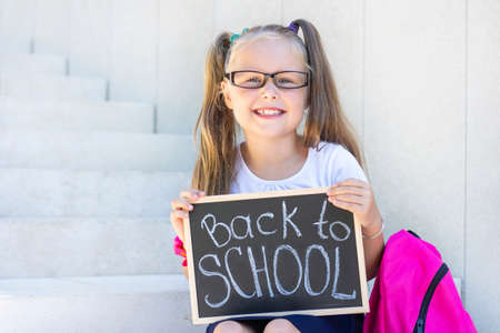 schoolgirl with glasses sits on the stairs, school backpack. Holds a sign in his hands with the inscription back to schoolの写真素材