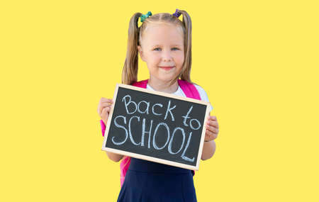 schoolgirl holds a sign with the words Back to school in her hands. isolate on yellow background