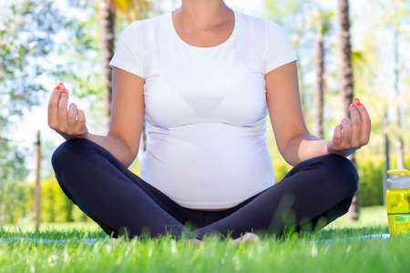 pregnant girl doing yoga in the park. girl in white t-shirt sits in lotus positionの写真素材