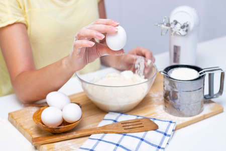 making dough for bread or homemade baked goods. ingredients on the desk. female hands holding an eggの写真素材
