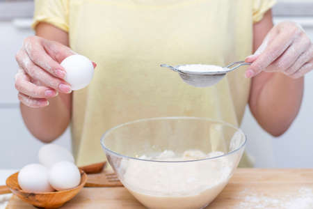 making dough for bread or homemade baked goods. ingredients on the desk. female hands holding an egg
