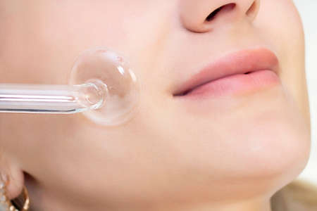 Cosmetologist performs a pulse current procedure for the face of a young woman. close