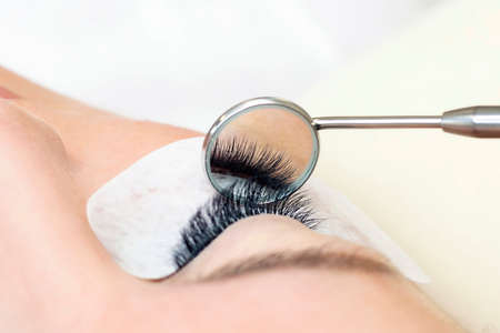 Eyelash extension procedure. Female eye with long eyelashes. Close up. mirror in the hands of the masterの写真素材