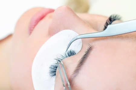 Eyelash extension procedure. Woman eye with long eyelashes. Close up. using tweezersの写真素材