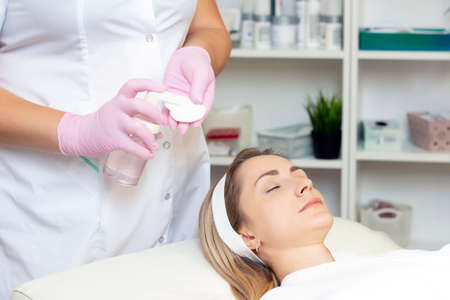 cosmetology. Close up picture of lovely young woman with closed eyes receiving facial cleansing procedure in beauty salon.の写真素材