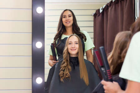 Womens hairdresser, beauty salon. hairdresser makes curls with a curling ironの写真素材