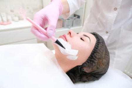 cosmetology. Close up picture of lovely young woman with closed eyes receiving facial cleansing procedure in beauty salon.の写真素材