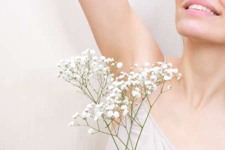 Young woman holding her hands up and showing armpits with gypsophila in her hand, armpits smooth transparent skin. The girl shows a clean armpit. Beauty portrait. Hair removal and depilation.の写真素材
