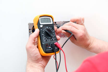 Electrician a wall socket with electronic multimeter. Wire and multimeter in hands close upの写真素材