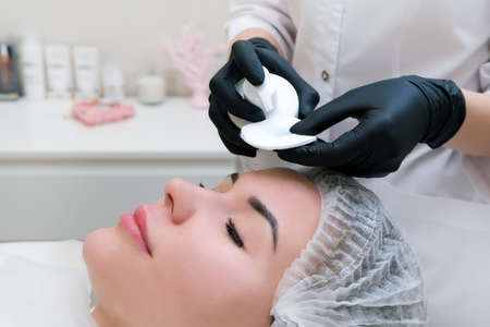 cosmetology. Close up picture of lovely young woman with closed eyes receiving facial cleansing...