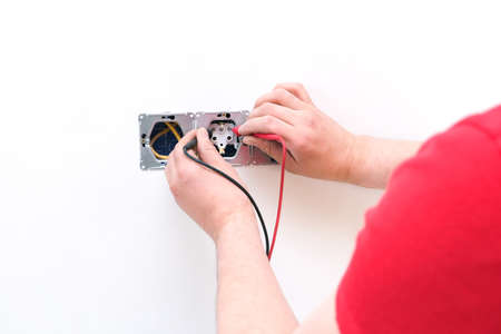 Electrician a wall socket with electronic multimeter. Wire and multimeter in hands close up