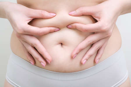 Fat belly of a woman. female hand of excessive fat on the belly. diet lifestyle concept to shrink belly and form healthy abdominal muscles.の写真素材
