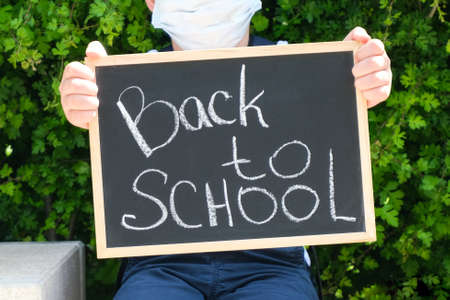 Schoolboy in a protective mask from the virus with a sign in his hands stands on the street on the...