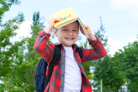A schoolboy with a book on his head is like a roof on the street on the way to school. Back to schoolの写真素材