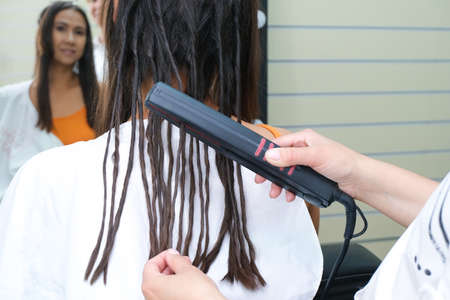 Young woman with dreadlocks. false dreadlocks on the curling iron. holds in hand and smiles