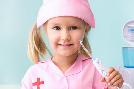 little girl in a nurses gown brushes her teeth using an irrigator. girl is brushing her teeth with a stream of water from an irrigator.の写真素材