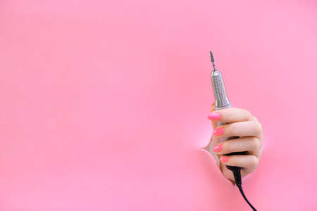 apparatus for manicure in the hand of a young woman on a pink background from a hole. hardwear manicure. copy spaceの写真素材