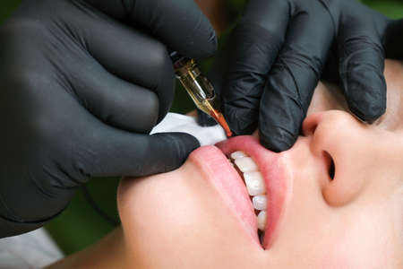 Young woman having permanent makeup on her lips at the beauticians salon. Natural green background. close upの写真素材