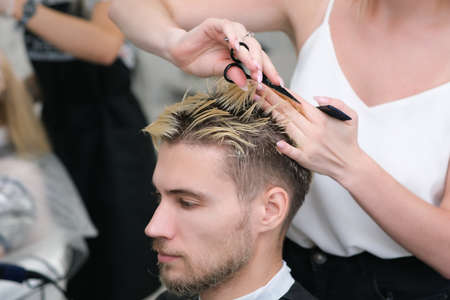 hairdresser cuts the hair of a young man with blond dyed hair with scissors in a beauty salon. Professional hair care.の写真素材