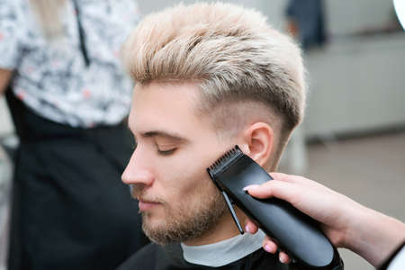 haircut process of blond young man with hair trimmer in armchair in barbershop salon, barbershop...