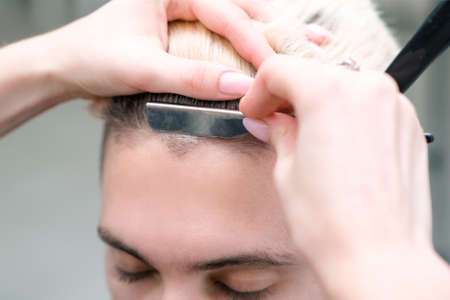straight razor. haircut process of blond young man in barbershop salon, barbershop concept for men and boysの写真素材