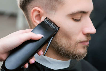 haircut process of blond young man with hair trimmer in armchair in barbershop salon, barbershop...