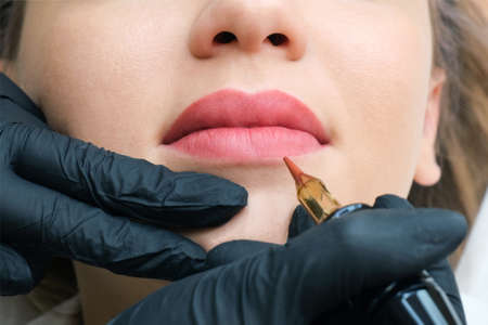 Young woman having permanent makeup on her lips at the beauticians salon. Natural green backgroundの写真素材