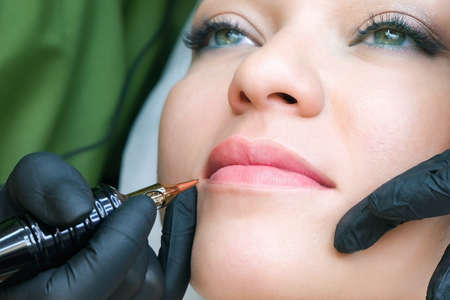 Young woman having permanent makeup on her lips at the beauticians salon. Natural green backgroundの写真素材