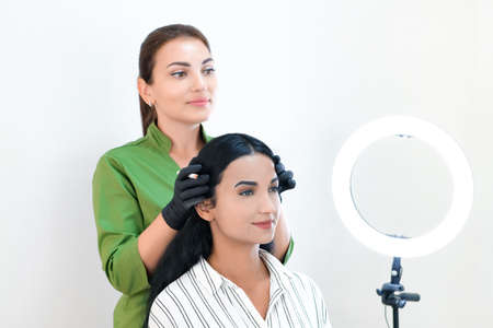 Beautician makes permanent eyebrow makeup on the face of a beautiful young woman