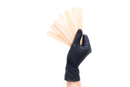 hand in a black glove holds wooden sticks for depilation on white isolated background