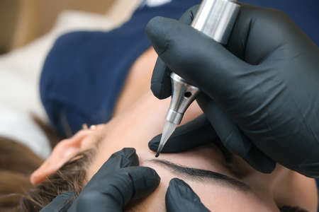 Beautician makes permanent eyebrow makeup on the face of a beautiful young woman. Permanent eyebrow...
