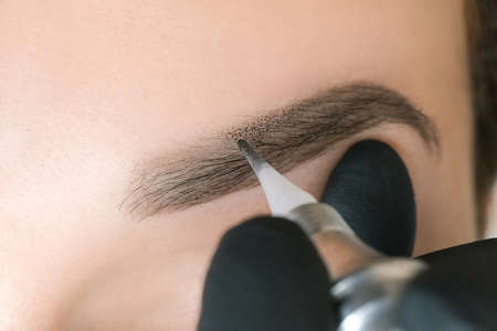 Beautician makes permanent eyebrow makeup on the face of a beautiful young woman. Permanent eyebrow...