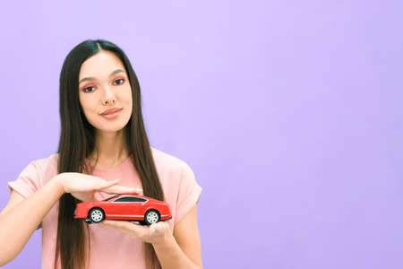 Driving school idea and concept, student driver passed the exam, drivers license, portrait of a beautiful happy young woman, holding a car in her hand. on a purple isolated background. place for your text, copyspaceの写真素材