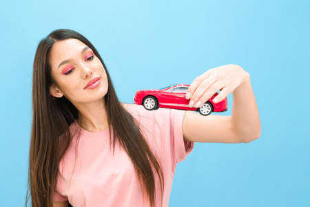 Driving school idea and concept, student driver passed the exam, drivers license, portrait of a beautiful happy young woman, holding a car in her hand. on a blue background. text, copyspaceの写真素材