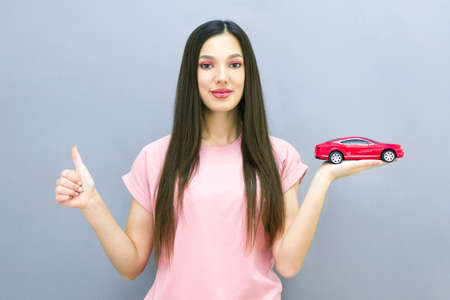 Driving school idea and concept, student driver passed the exam, drivers license, portrait of a young woman, holding a car in her hand. on a gray background. place for text, copyspace. shows likeの写真素材